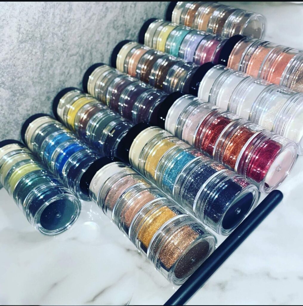 Stacked mineral pigment jars and brush showcasing loose powder eyeshadows by Siol Beauty on white background.